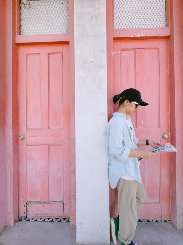 Woman in hat reading newspaper by pink doors